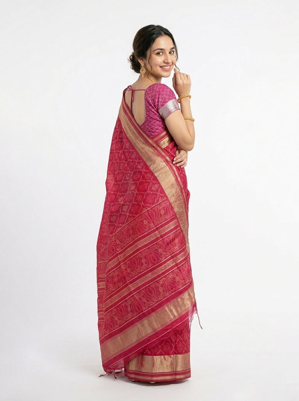 Woman in a red saree standing against a brick wall with plants