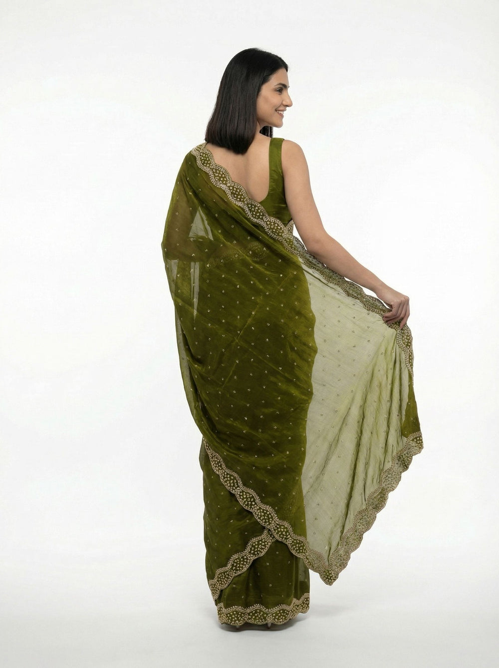 Woman in a green saree with gold border standing in an ornate architectural setting.