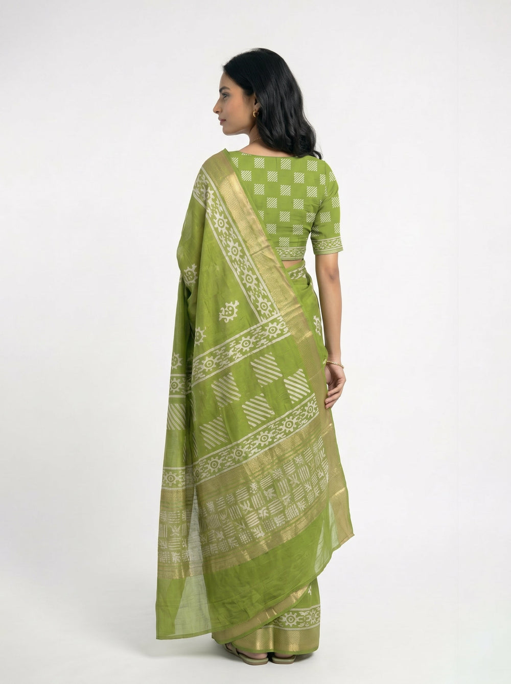 Woman in a green saree holding flowers, standing indoors with large windows.