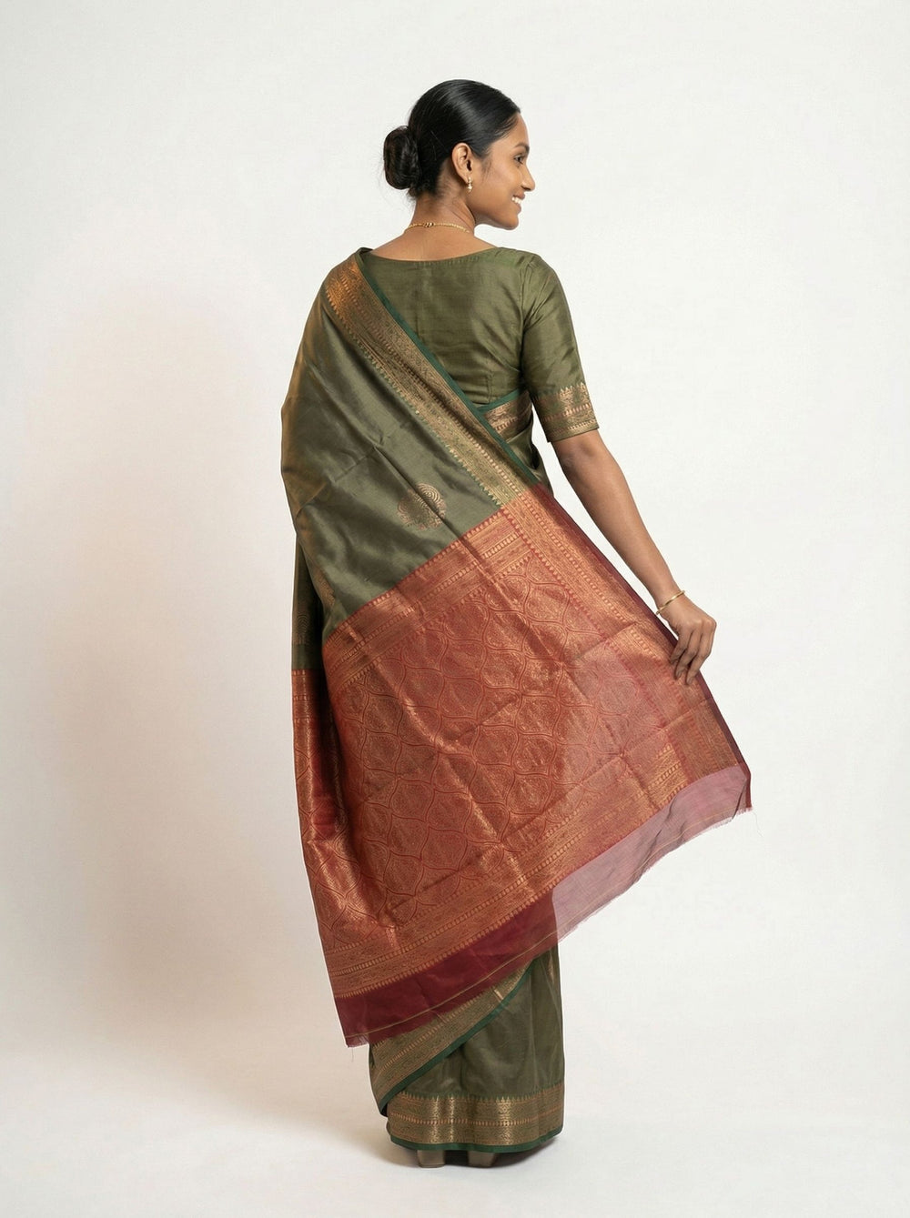 Woman in a traditional saree standing in a room with wooden furniture and decor.