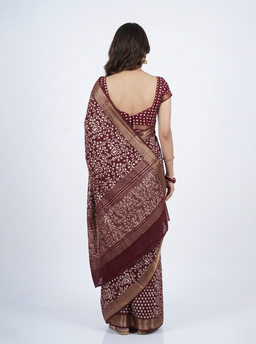 Woman in a patterned saree standing against a pink wall with rustic decor.