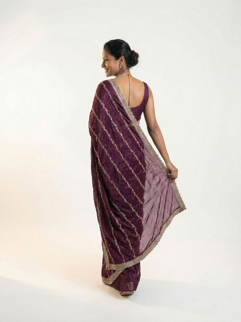 Woman in a purple saree standing outdoors with greenery and a bench in the background