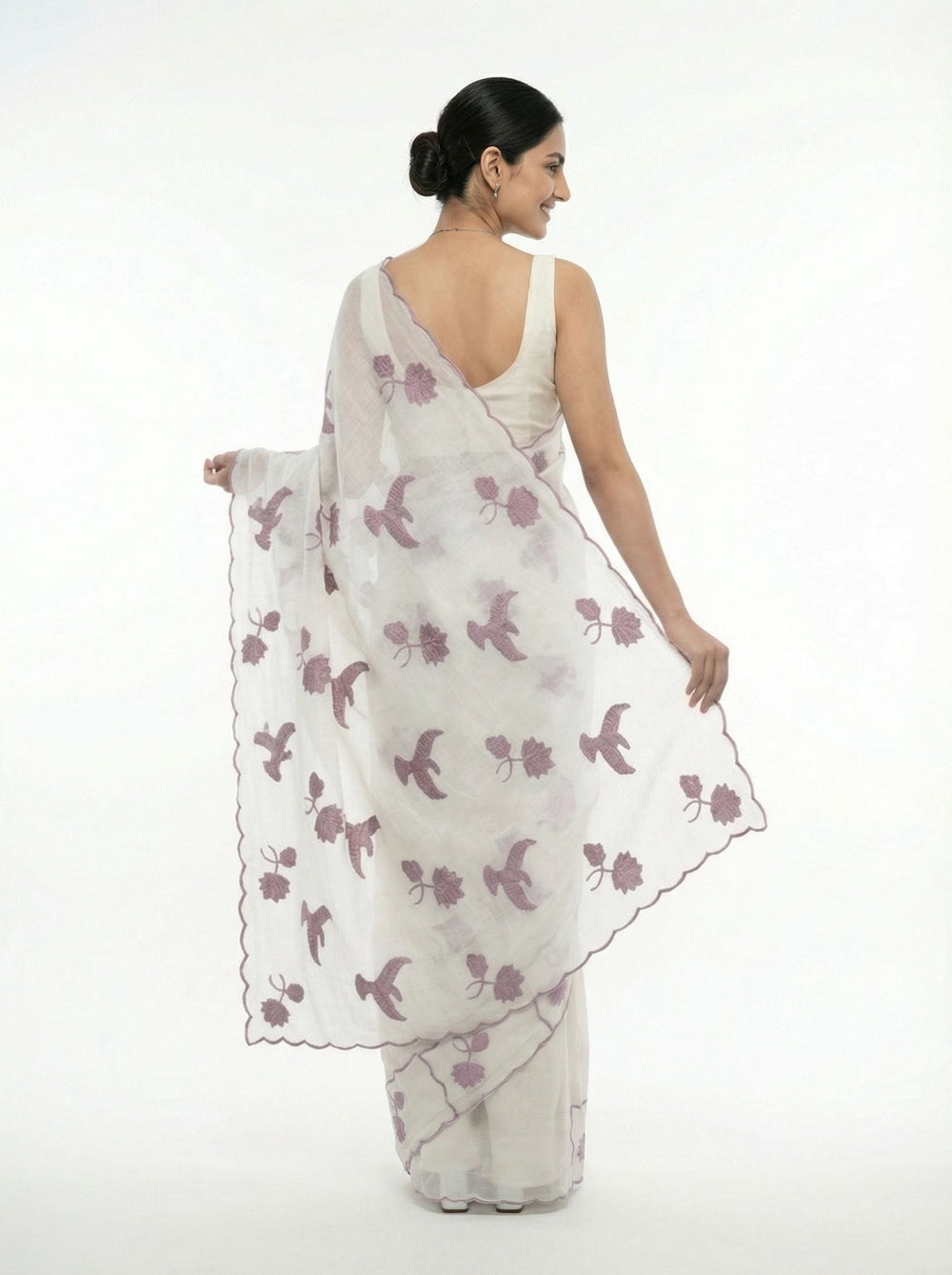 Woman in a white saree with purple floral patterns standing in a garden setting.