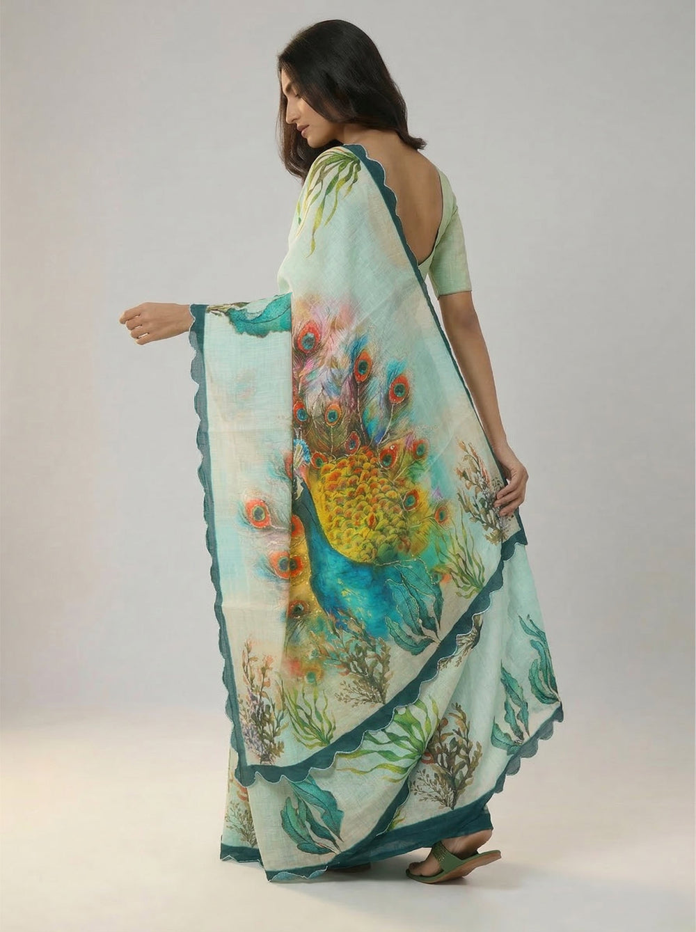 Woman in a light green saree with floral patterns standing in a room with a wooden cabinet and decorative items.