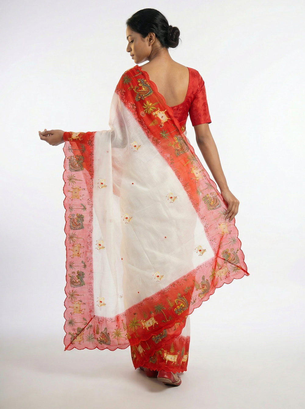 Woman in a white and red saree standing in an elegant room with decor.