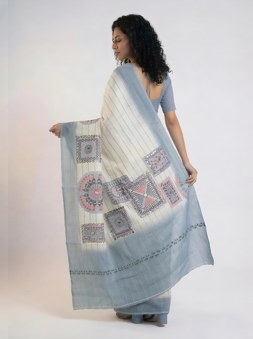 Woman in a saree standing in a room with wooden bookshelf and window