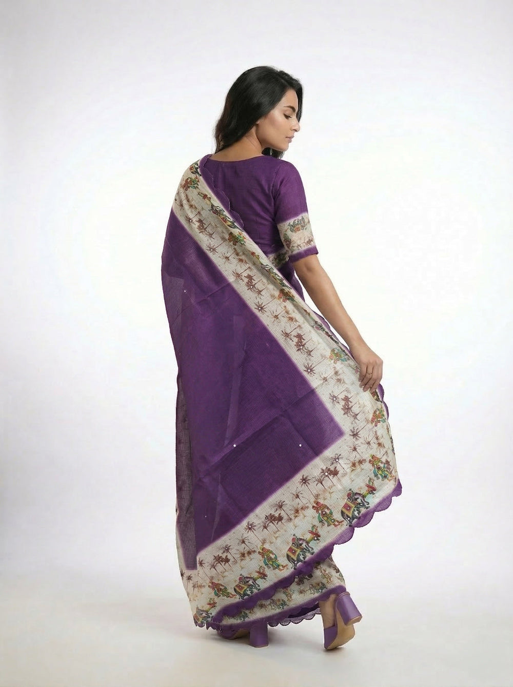 Woman in a purple saree standing in a room with decorative elements.