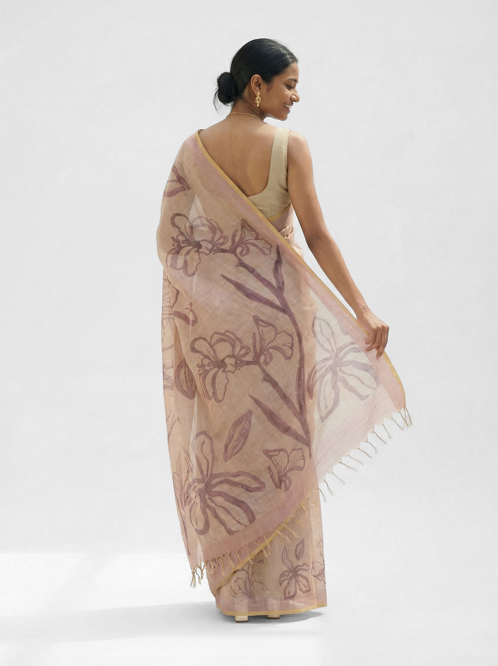 Woman in a traditional saree standing in an outdoor setting with plants and architectural elements.