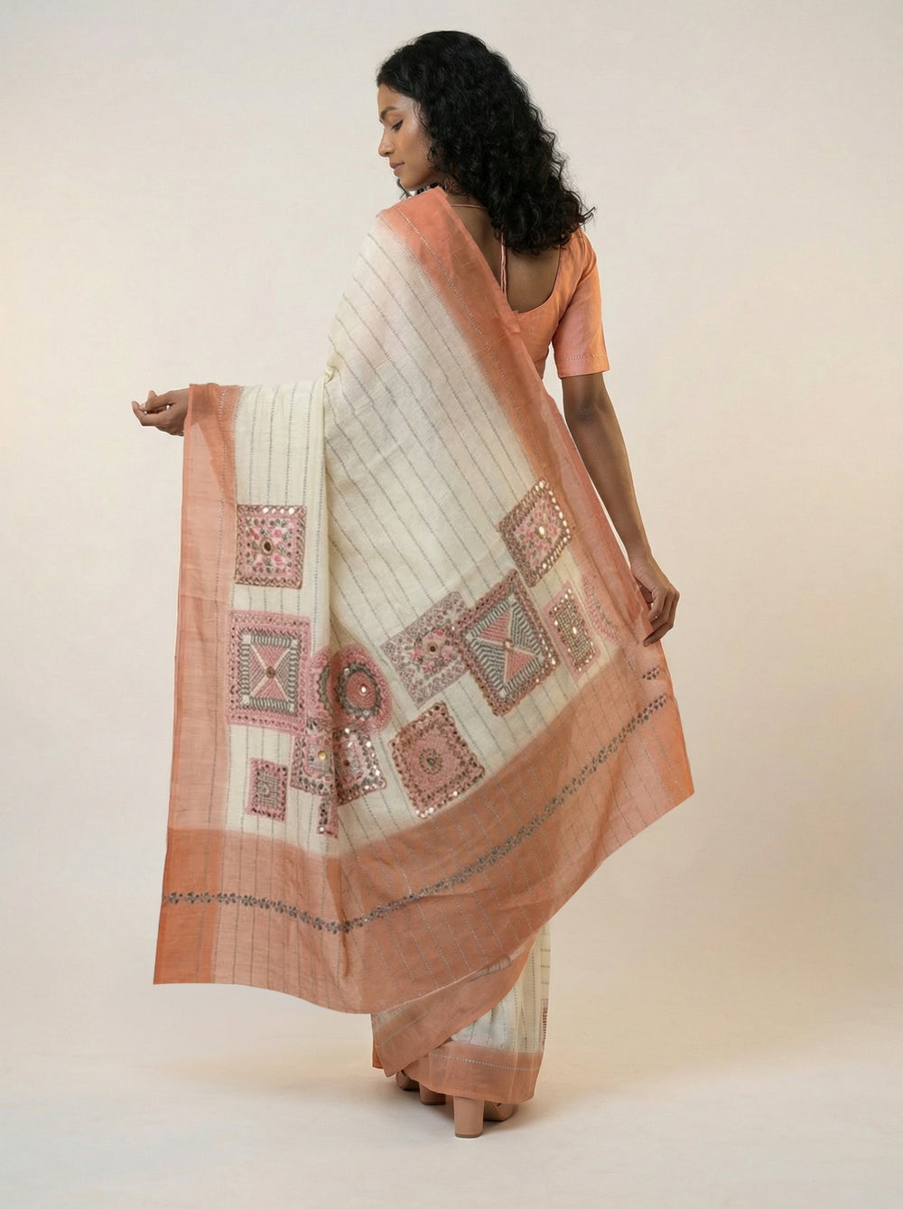 Woman in a saree standing in a room with a desk, lamp, and plant.