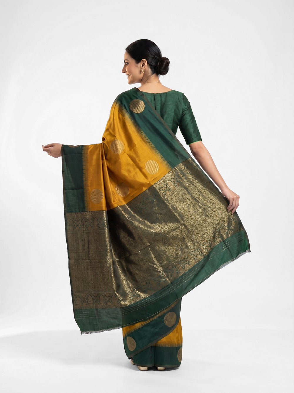 Woman in a green and yellow saree standing in a room with a decorative table and mirror.