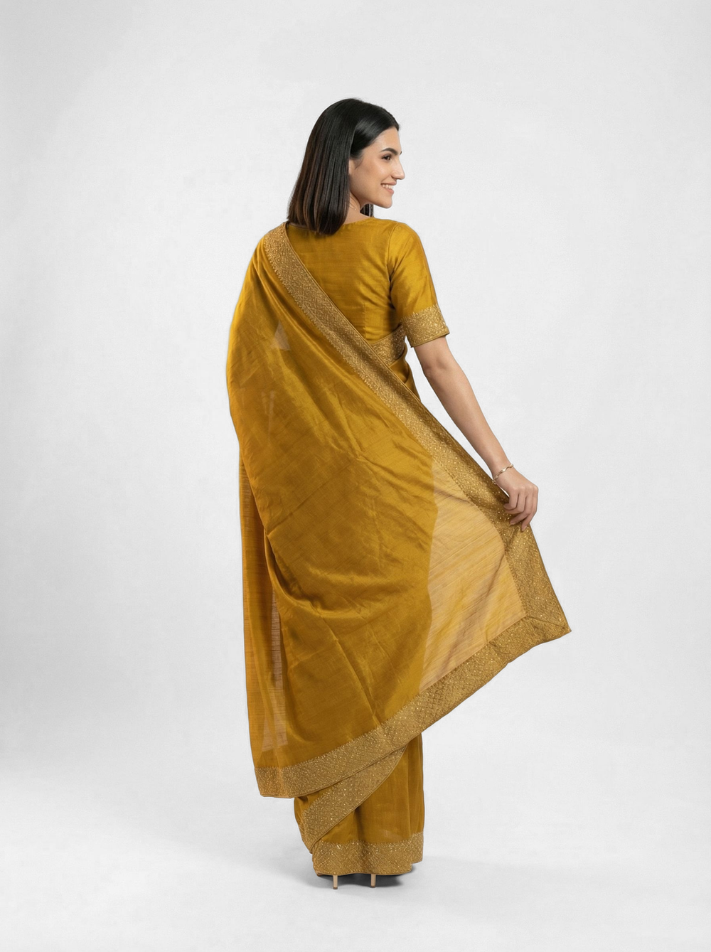 Woman in a yellow saree standing next to a potted plant with flowers in an outdoor setting.