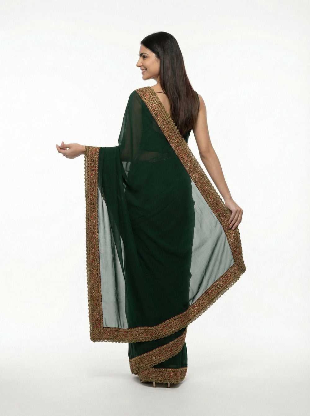 Woman in a green saree with gold border standing in an outdoor setting with flowers and columns.