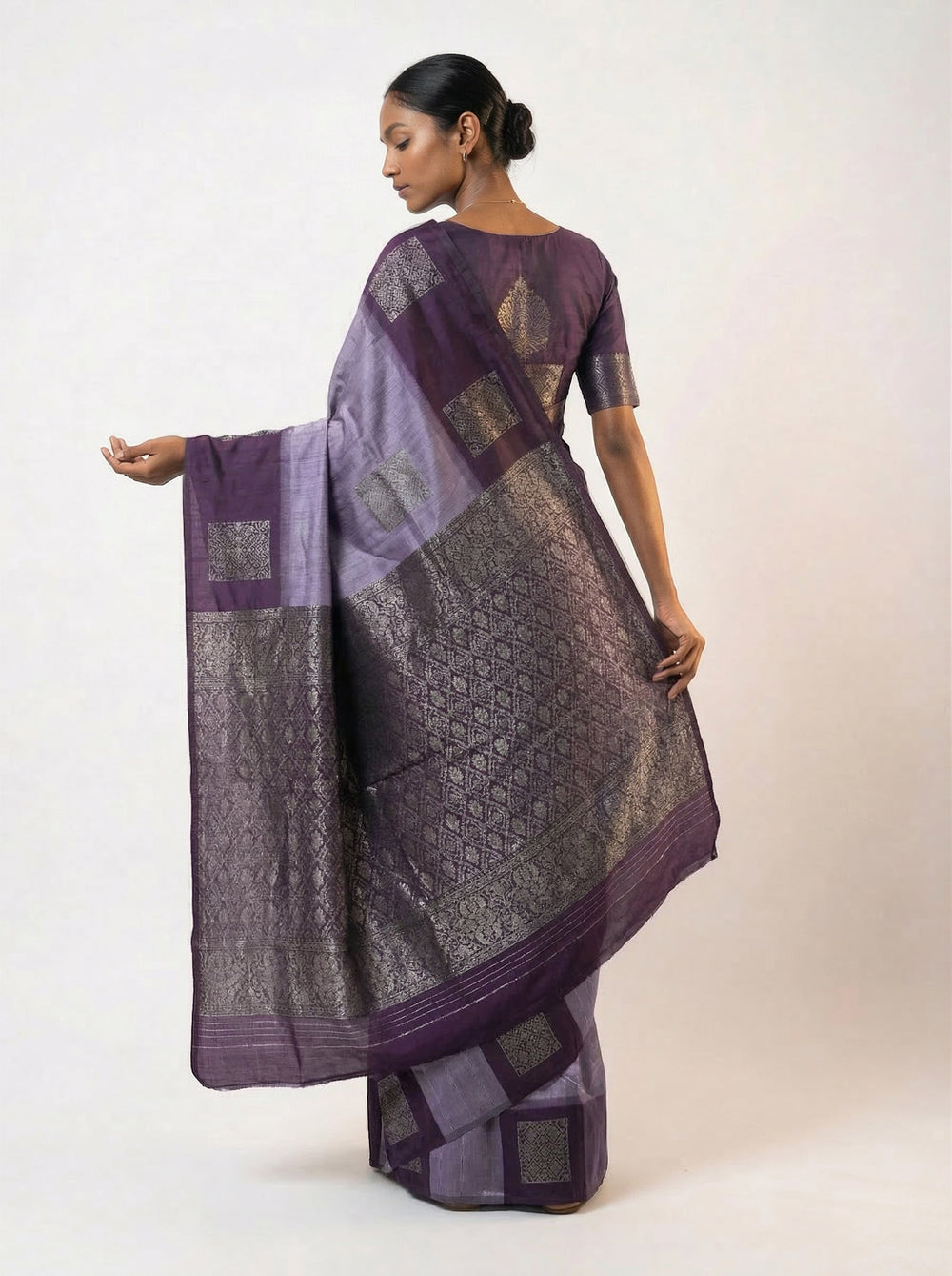 Woman wearing a purple saree with a subtle pattern on a peach background