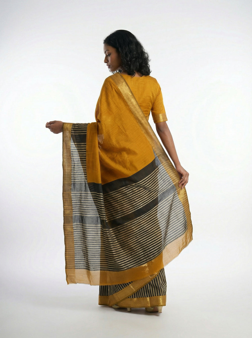 Woman in a mustard yellow saree standing against a textured wall.