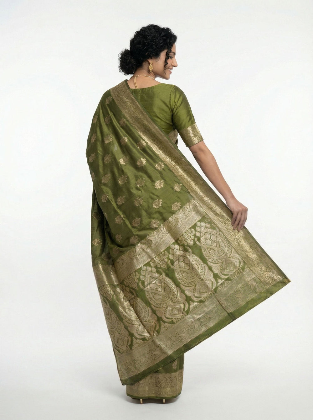 Woman in a green saree standing on a balcony with plants and traditional architecture in the background