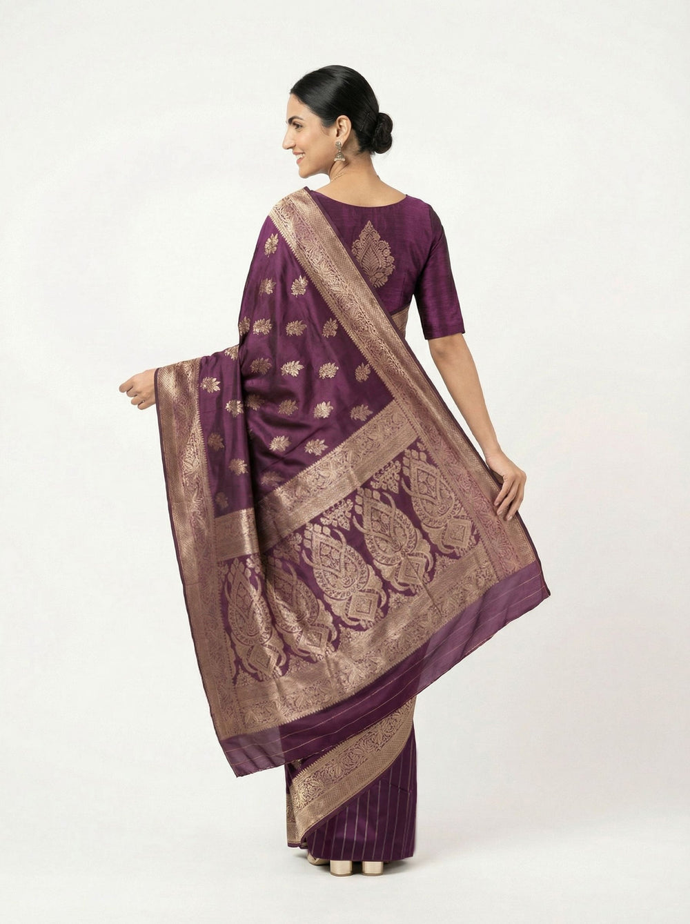 Woman in a purple saree standing in a room with a lamp and plant.