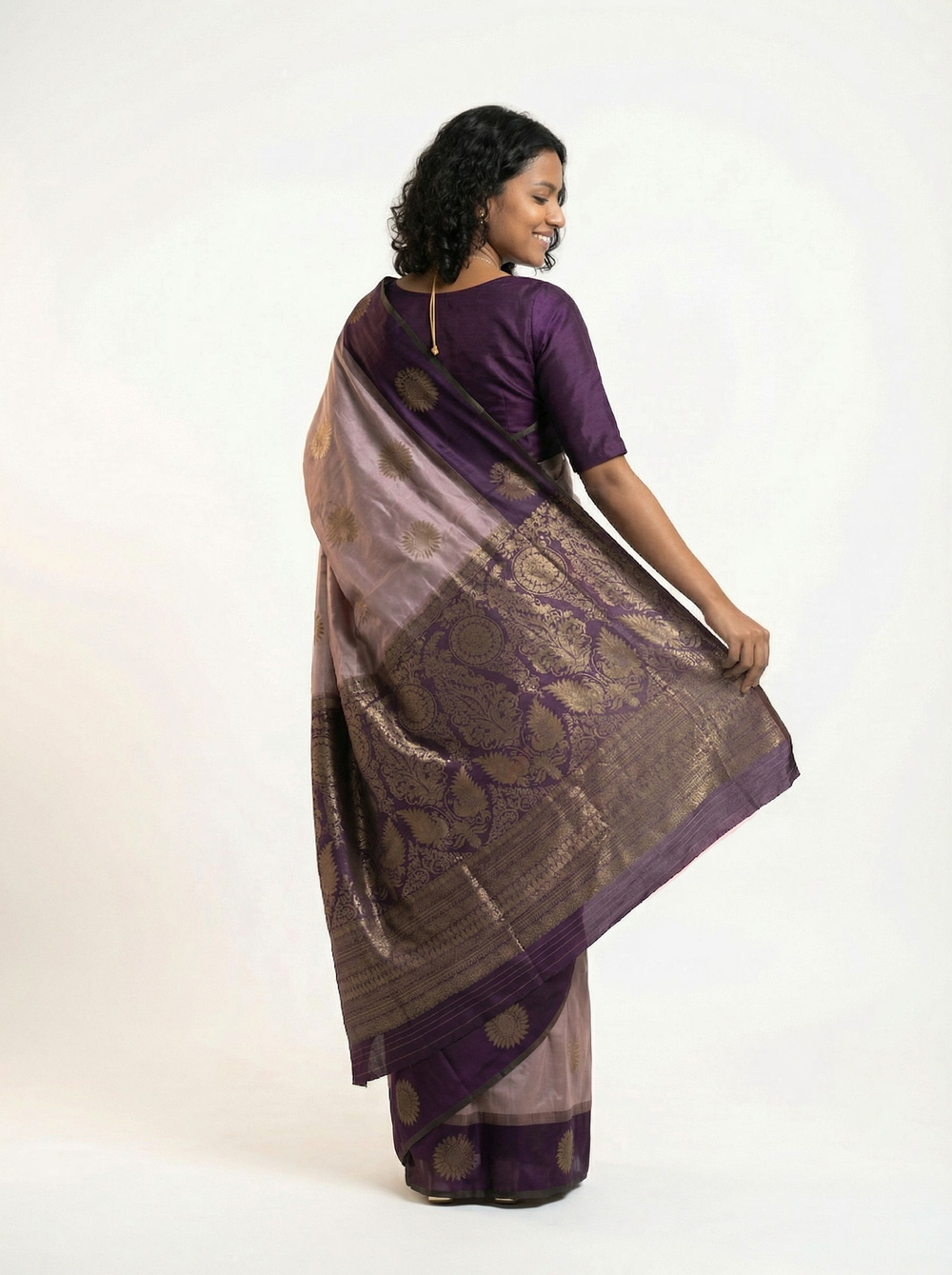 Woman in a purple and white saree standing by a window in a room with decor elements.
