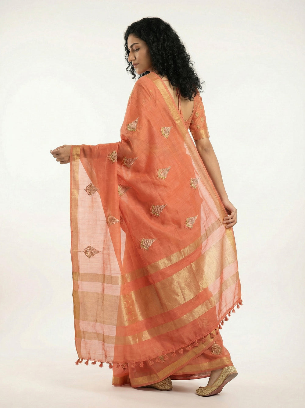 Woman in an orange saree standing on a balcony with plants and garden view