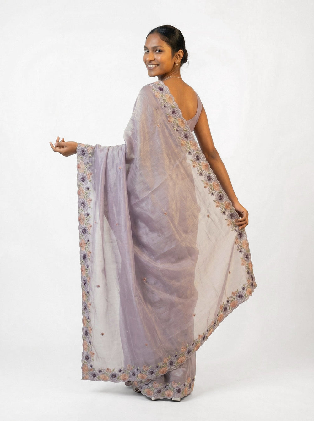 Woman in a lavender saree with floral patterns standing in an outdoor garden setting.