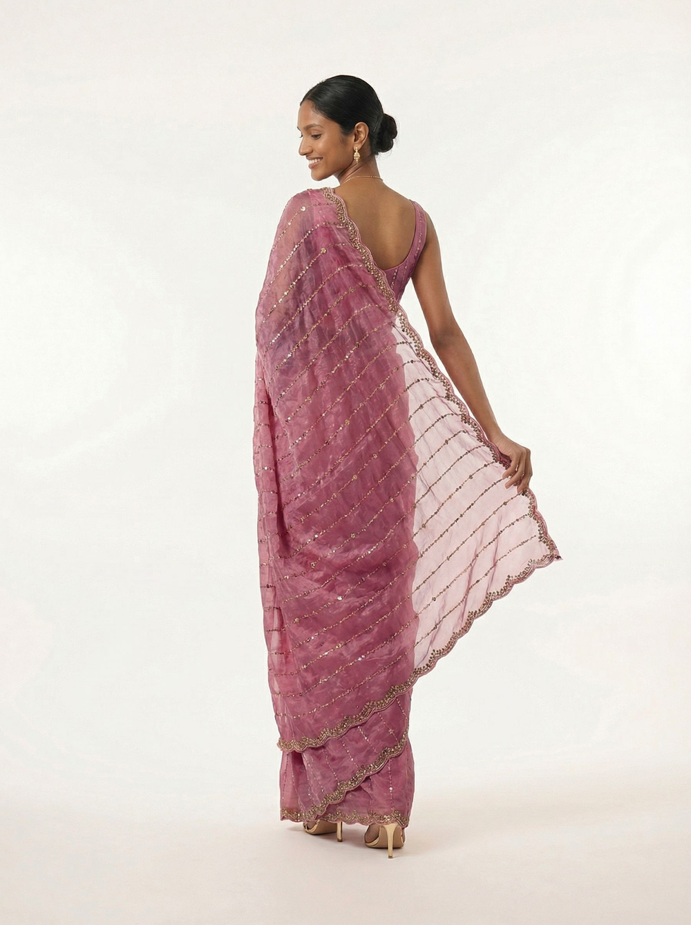 Woman in a pink saree standing in a courtyard with floral decorations.