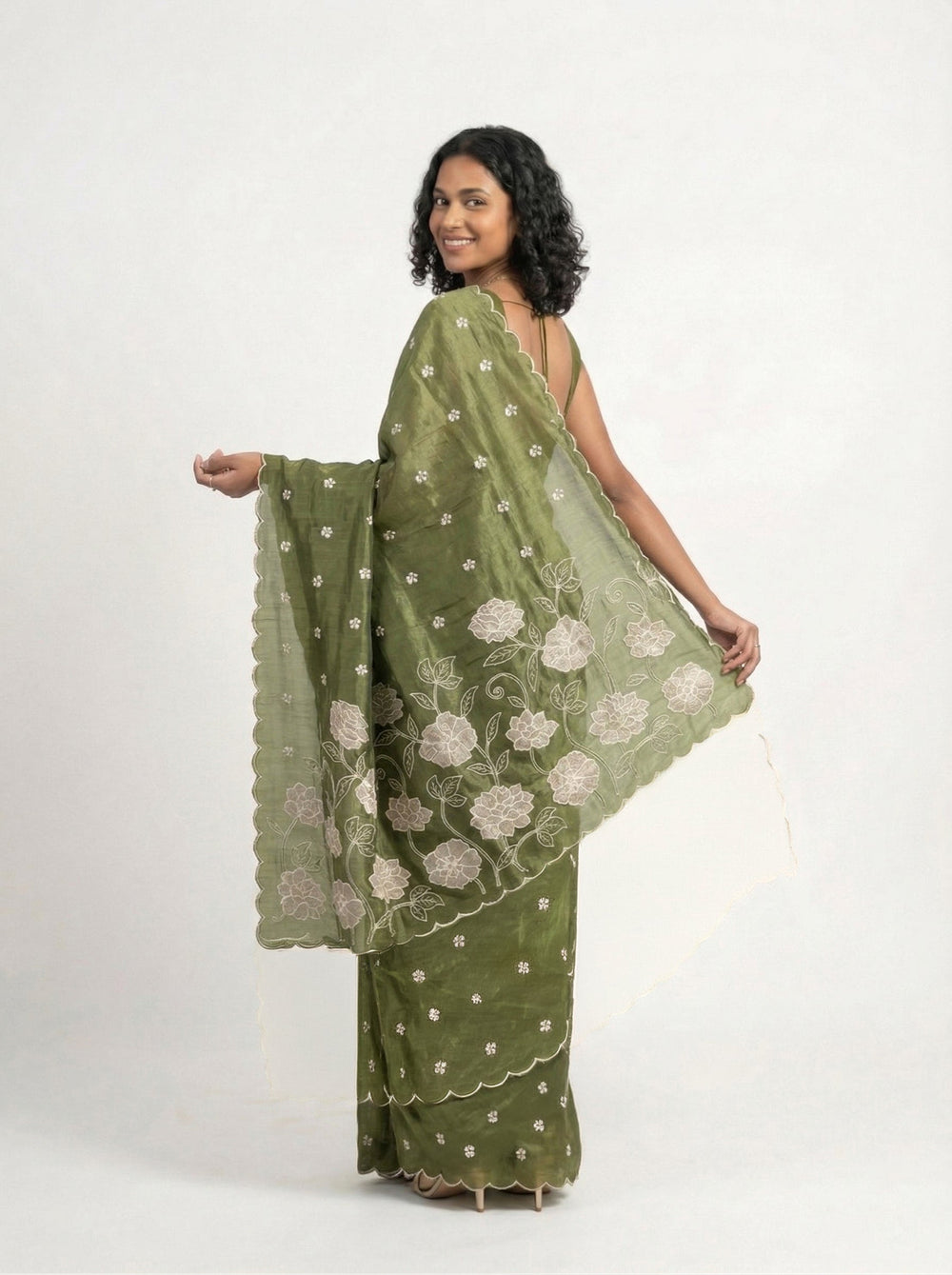 Woman in a green saree standing in a garden with plants and flowers around her.