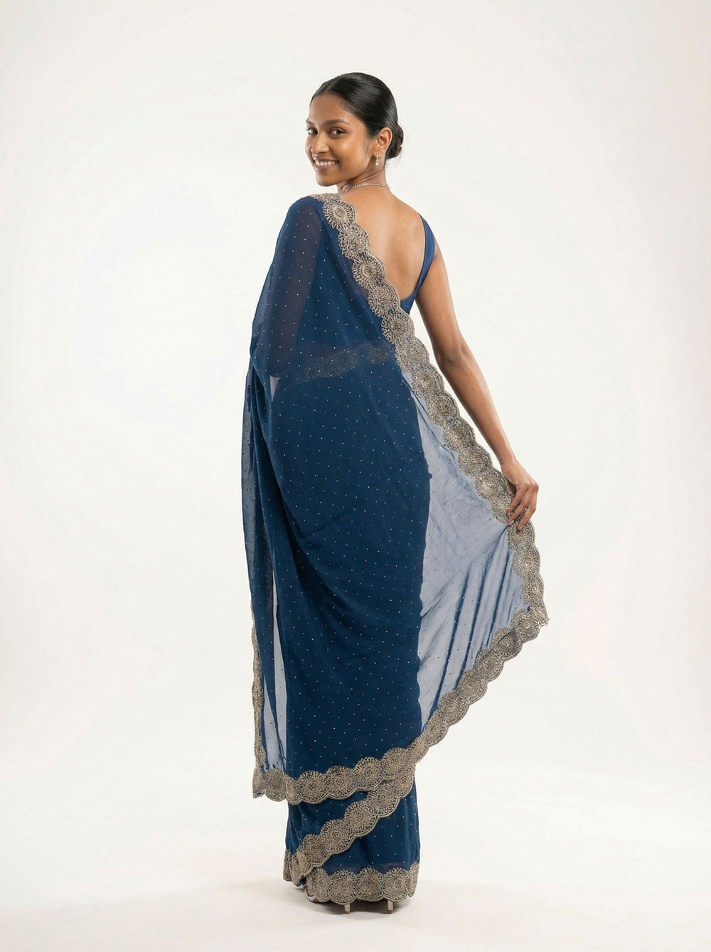 Woman in a blue saree standing in front of an old building with stone architecture.