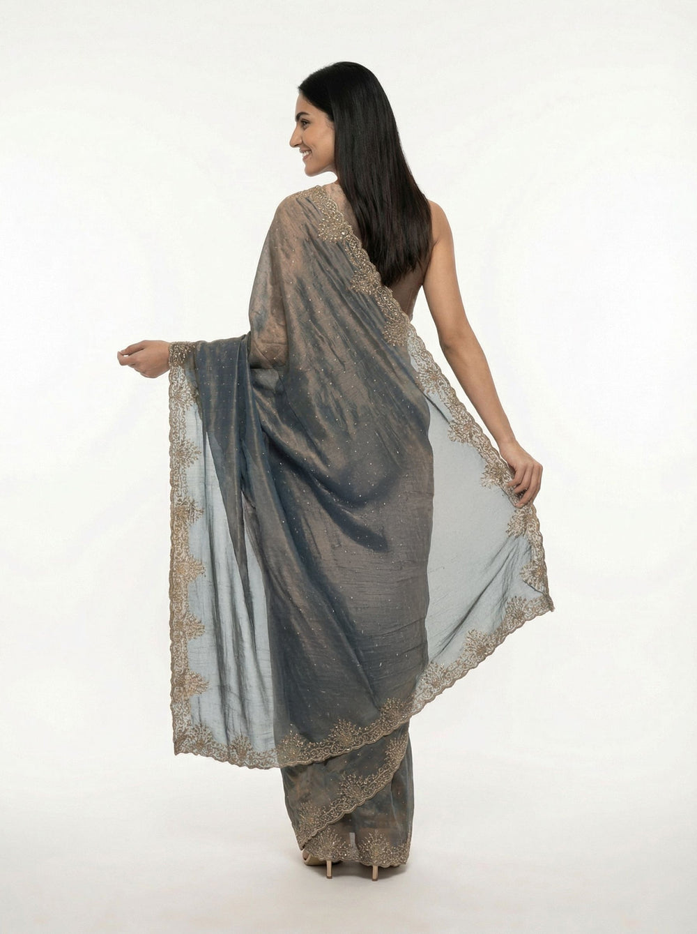 Woman in a traditional saree standing in an outdoor setting with architectural columns and greenery.