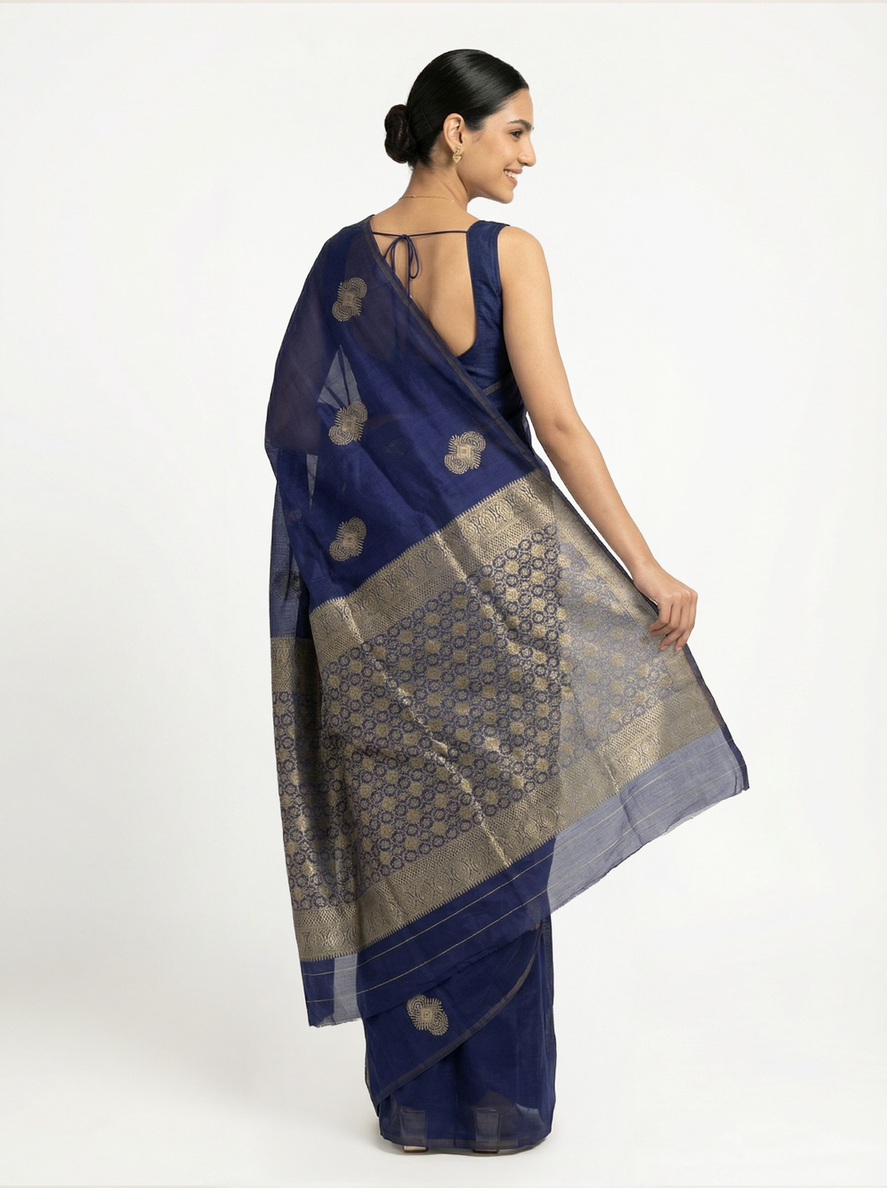 Woman in a blue saree standing in a room with a window and decorative items.