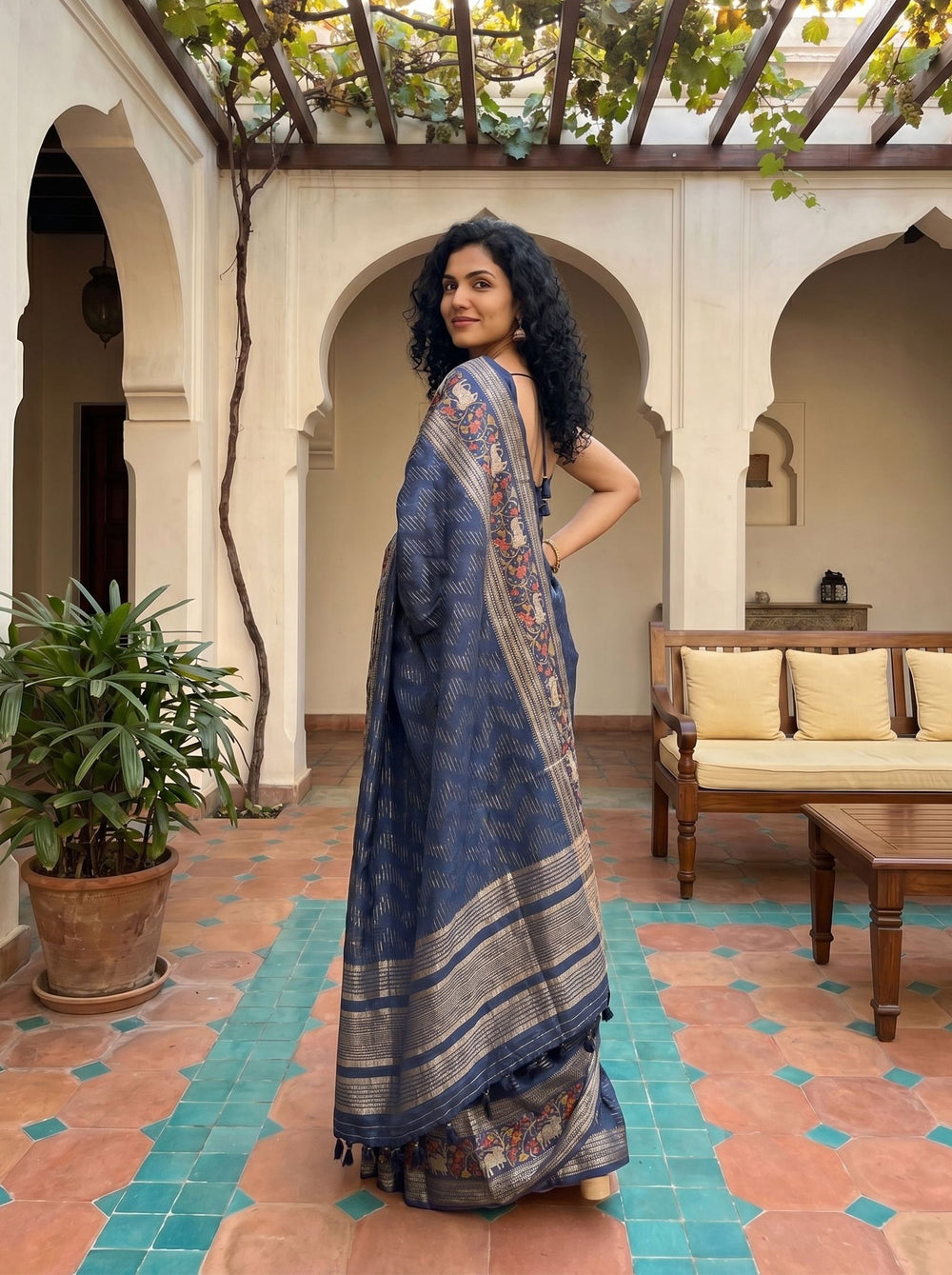 Woman in a blue saree with floral patterns standing in a courtyard.
