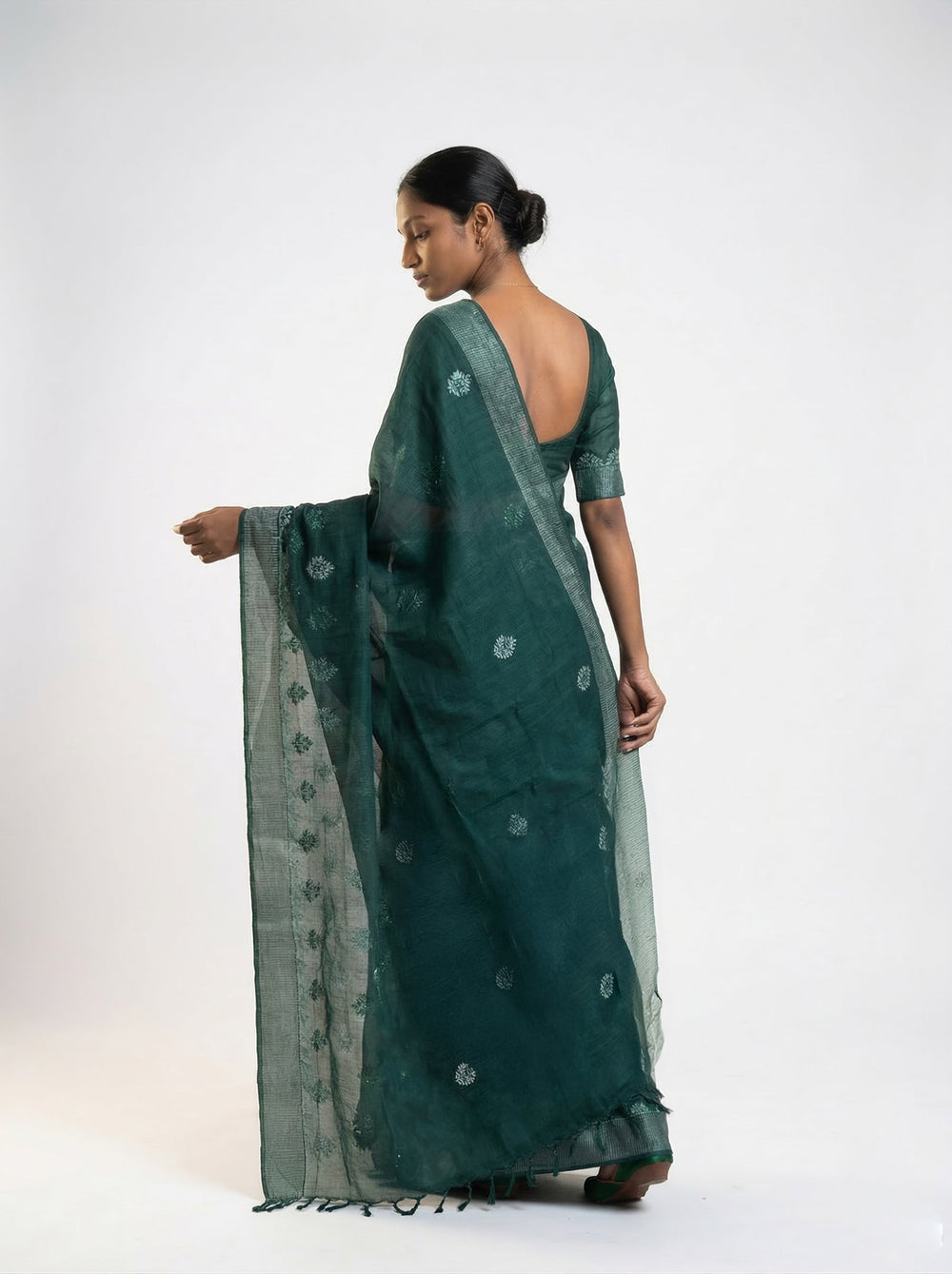 Woman in a green saree standing by a window in a room with decor elements.