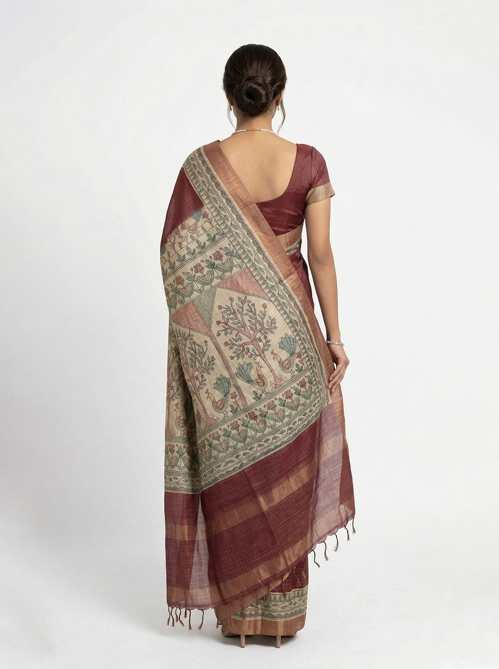 Woman in a traditional maroon saree with a floral pattern standing among greenery.