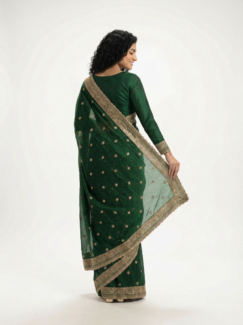 Woman in a green saree standing in an ornate courtyard with decorative arches and plants.