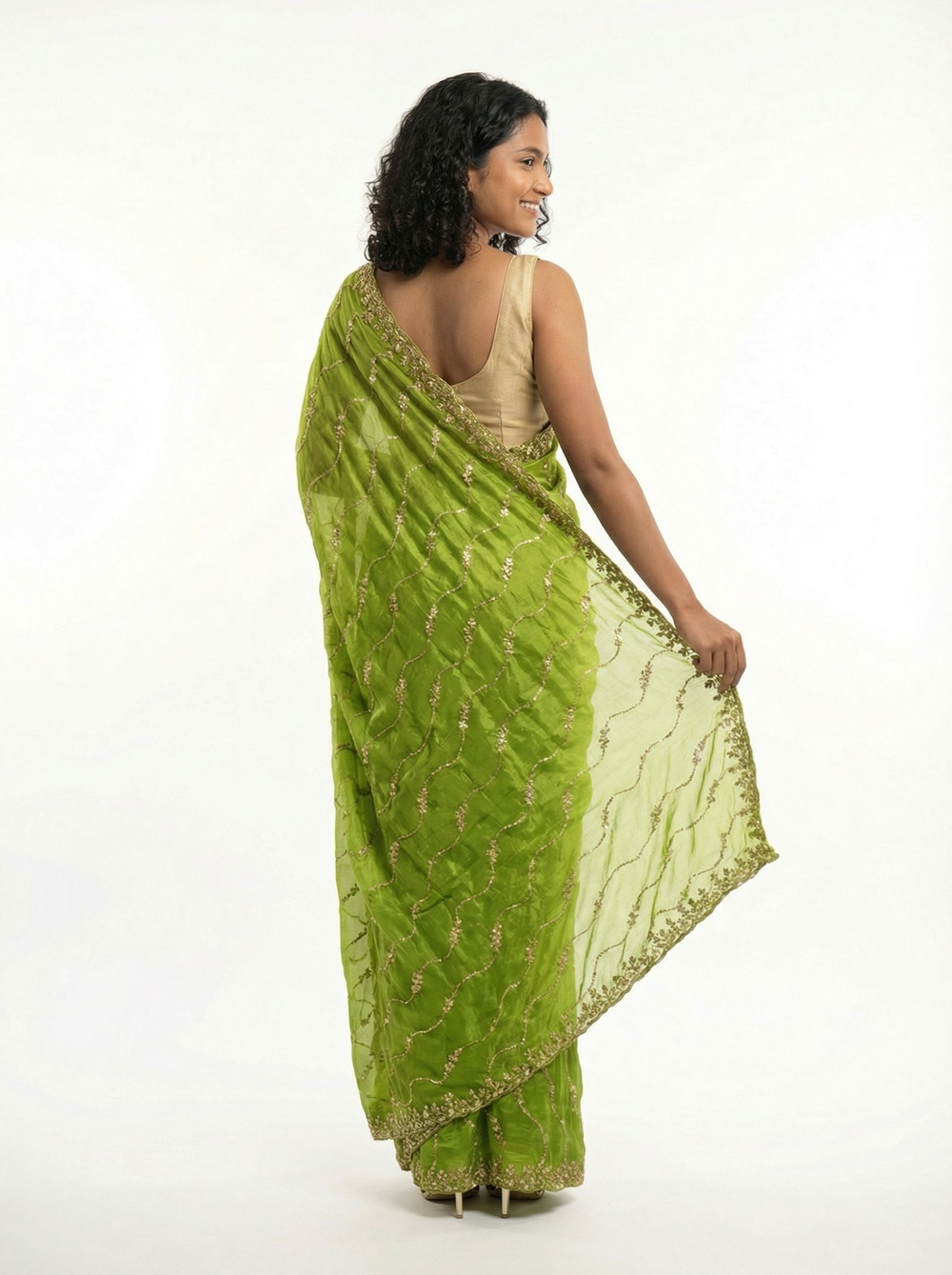 Woman in a green saree standing in front of a decorative building with flowers.