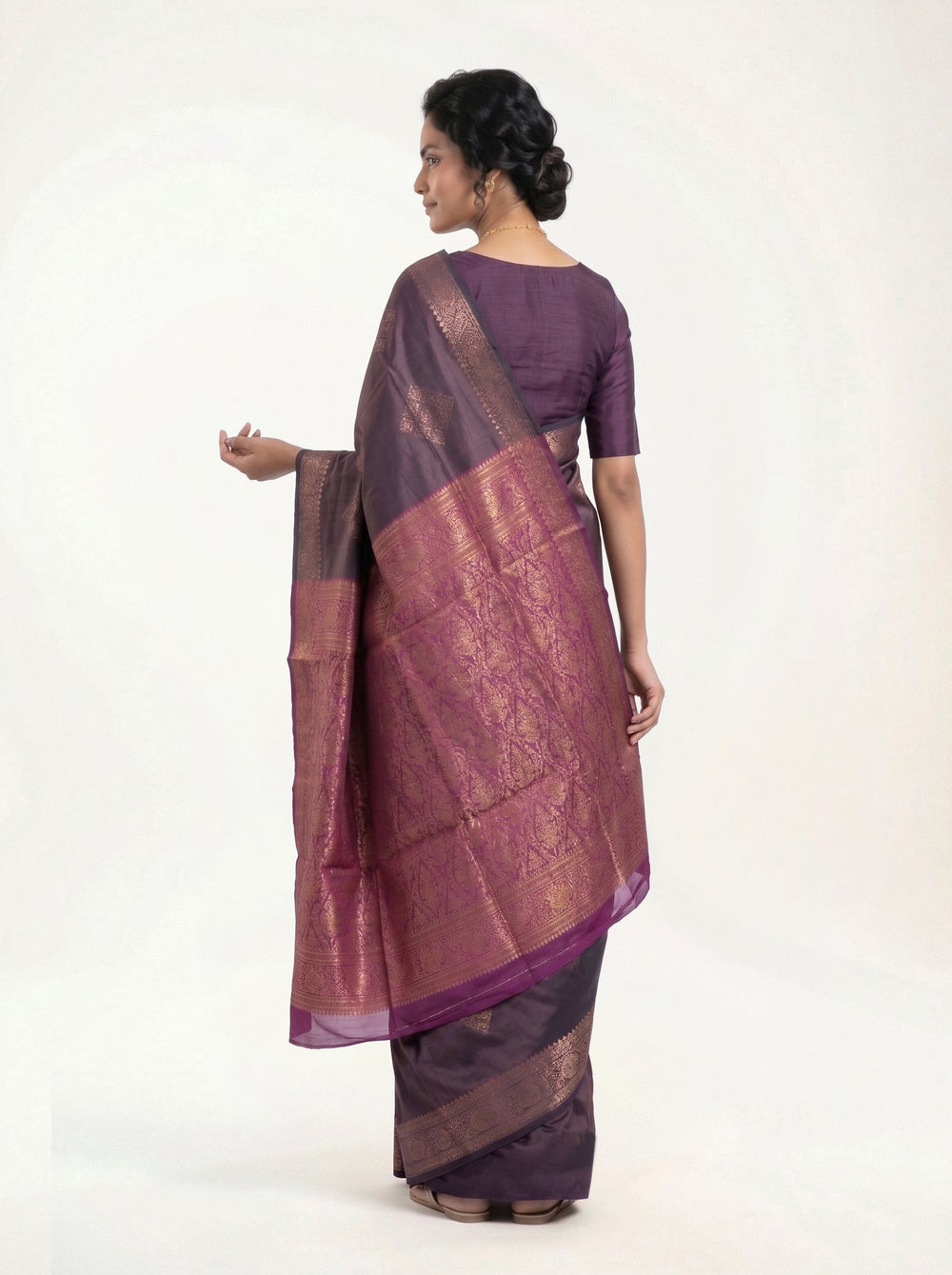 Woman in a purple saree sitting in a room with decor elements.