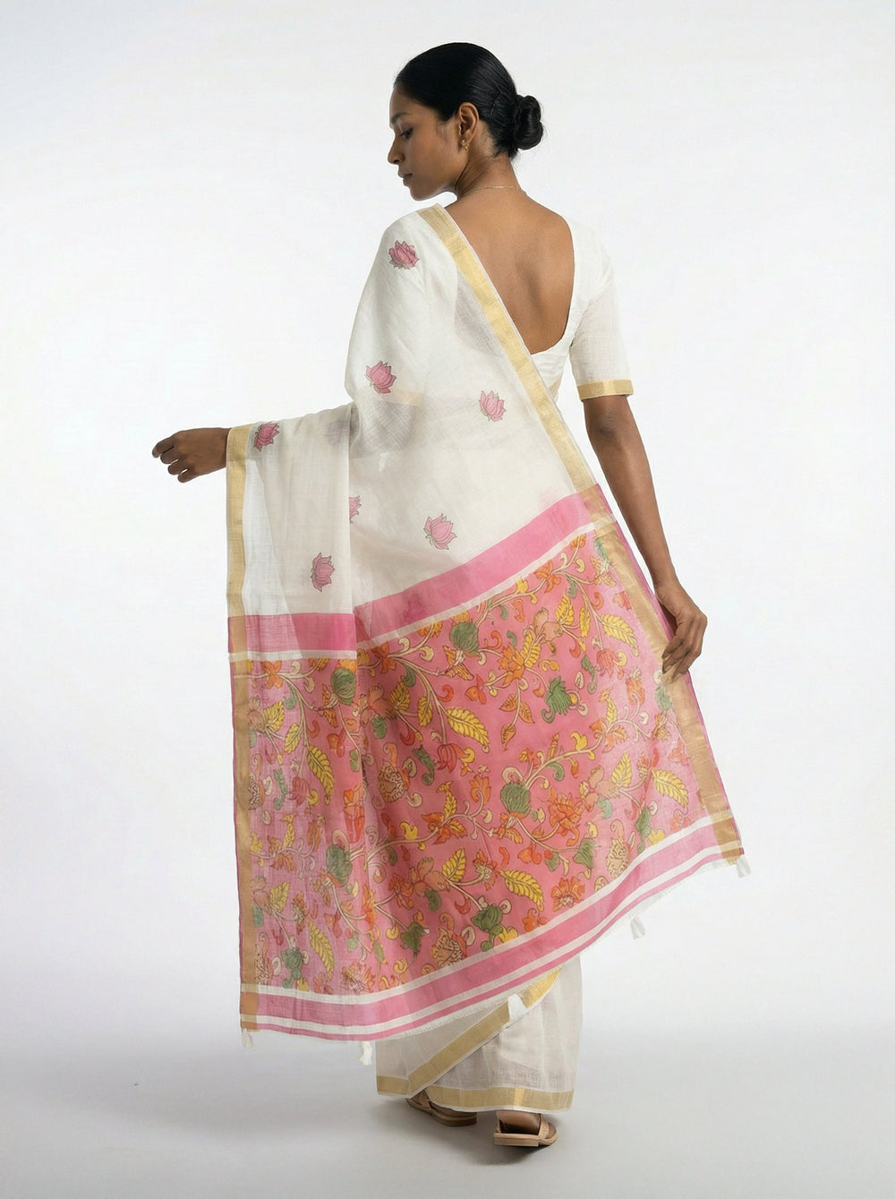 Woman in a white saree with pink border standing in a room with decor elements.