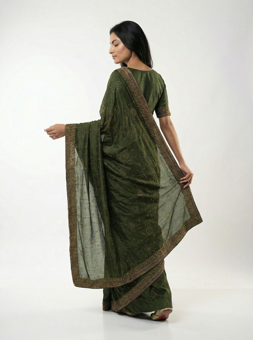 Woman in a green saree standing in an outdoor setting with plants and architectural elements.
