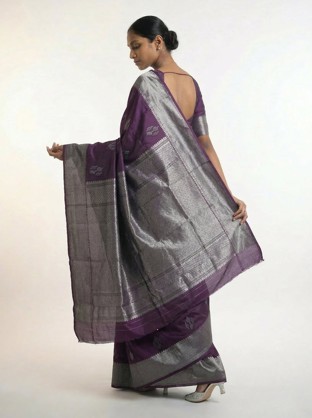 Woman wearing a purple saree with silver border against a pink background