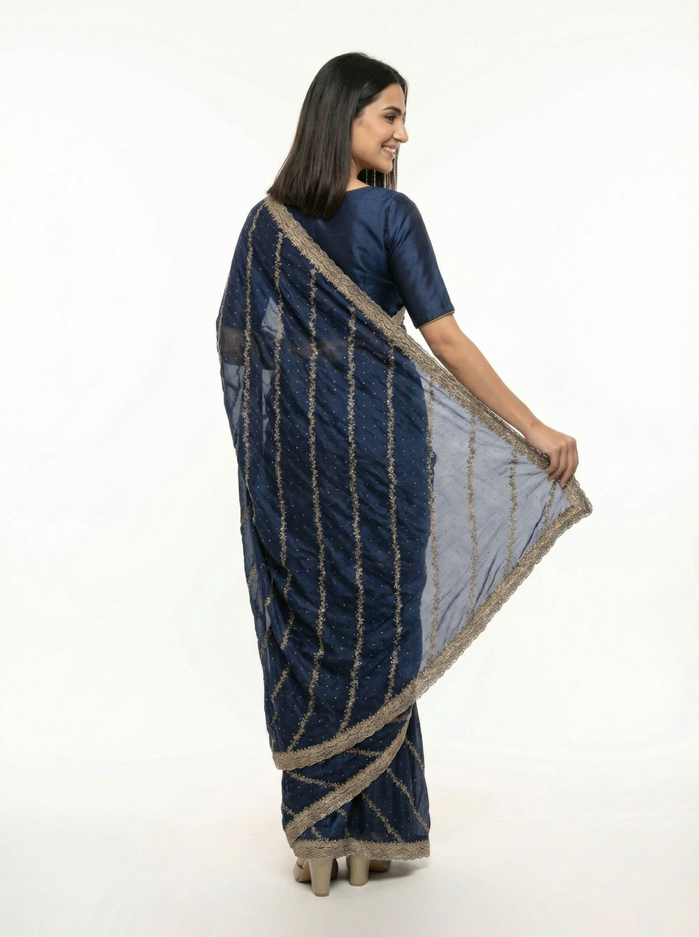 Woman in a blue saree standing in a decorative outdoor setting with plants and architectural elements.