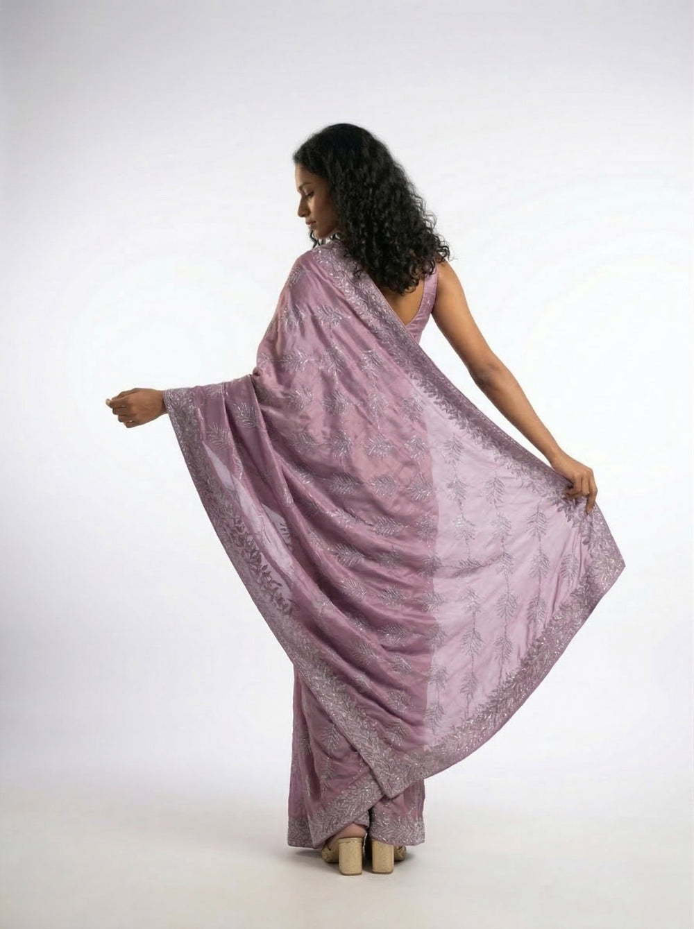 Woman in a pink saree standing in an outdoor setting with architectural columns and plants.