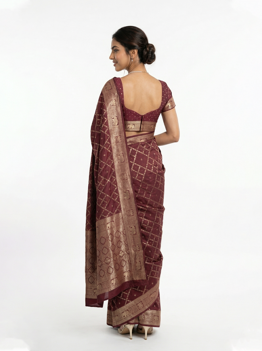 Woman in a maroon saree with gold patterns standing in an architectural setting.