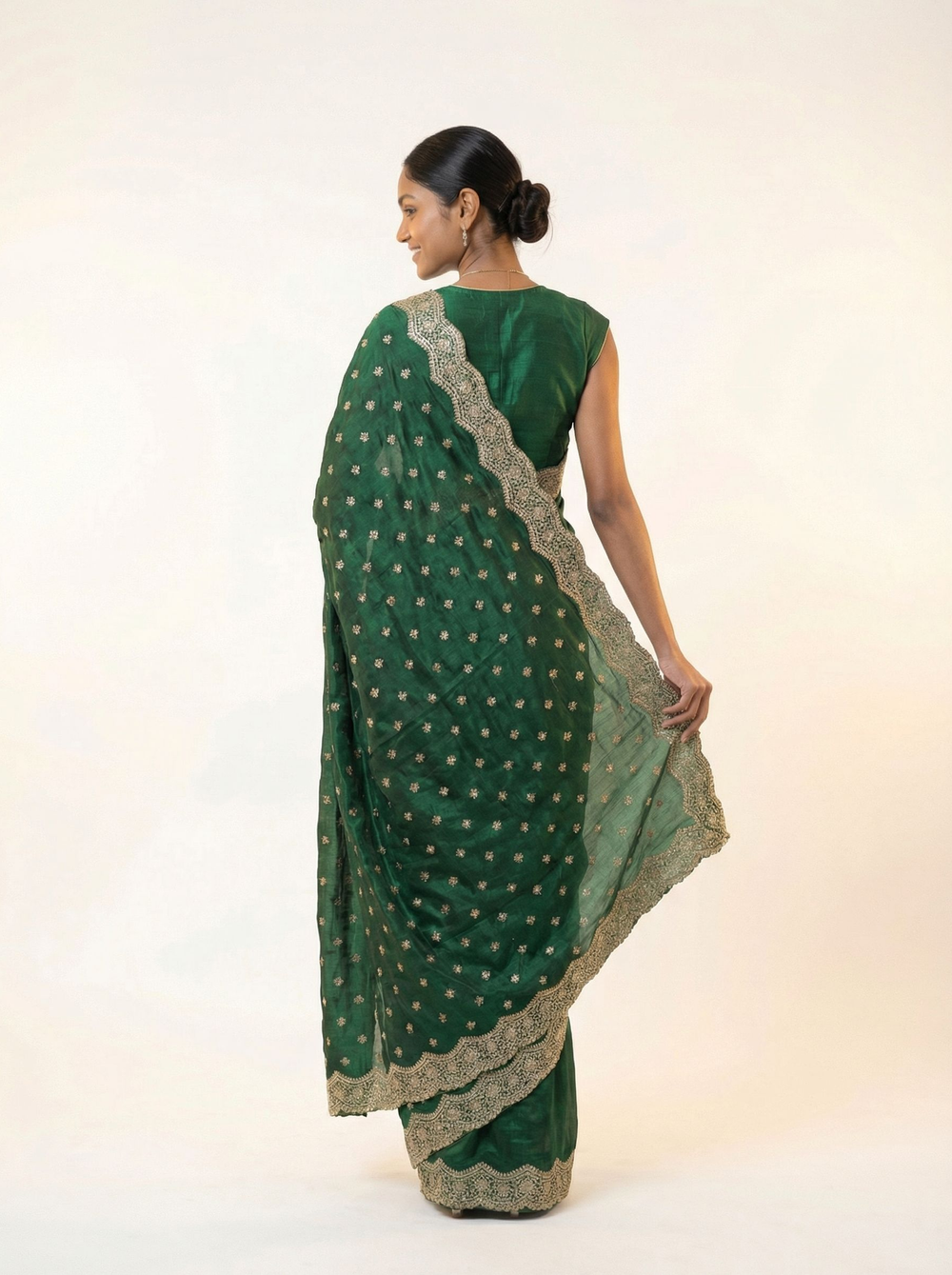 Woman in a green saree standing in an outdoor setting with plants and architectural elements.