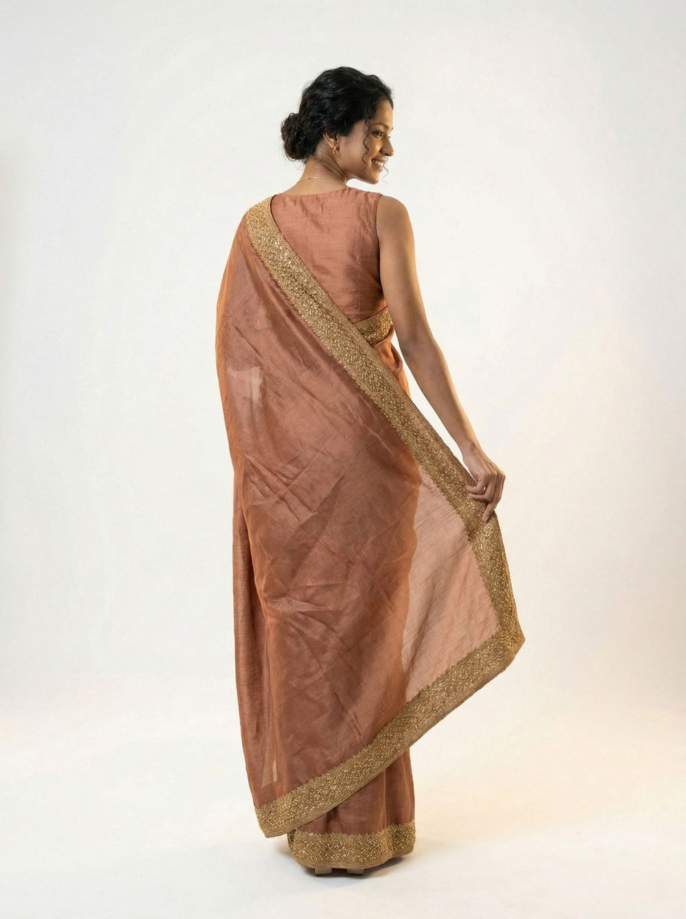 Woman in a traditional saree standing in an outdoor setting with stone architecture and greenery.