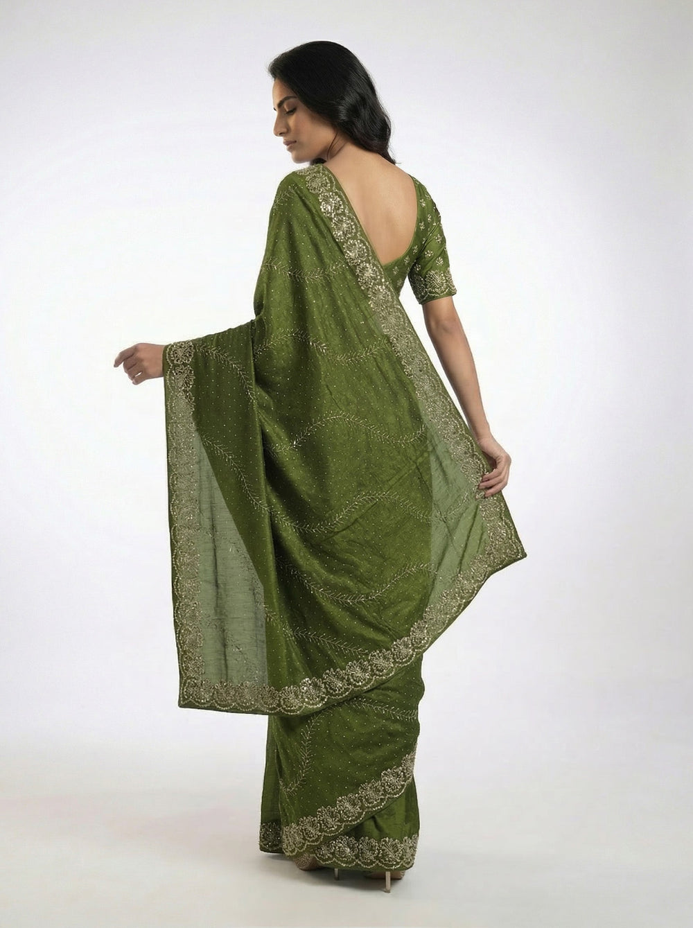 Woman in a green saree standing in an outdoor setting with plants and architectural elements.