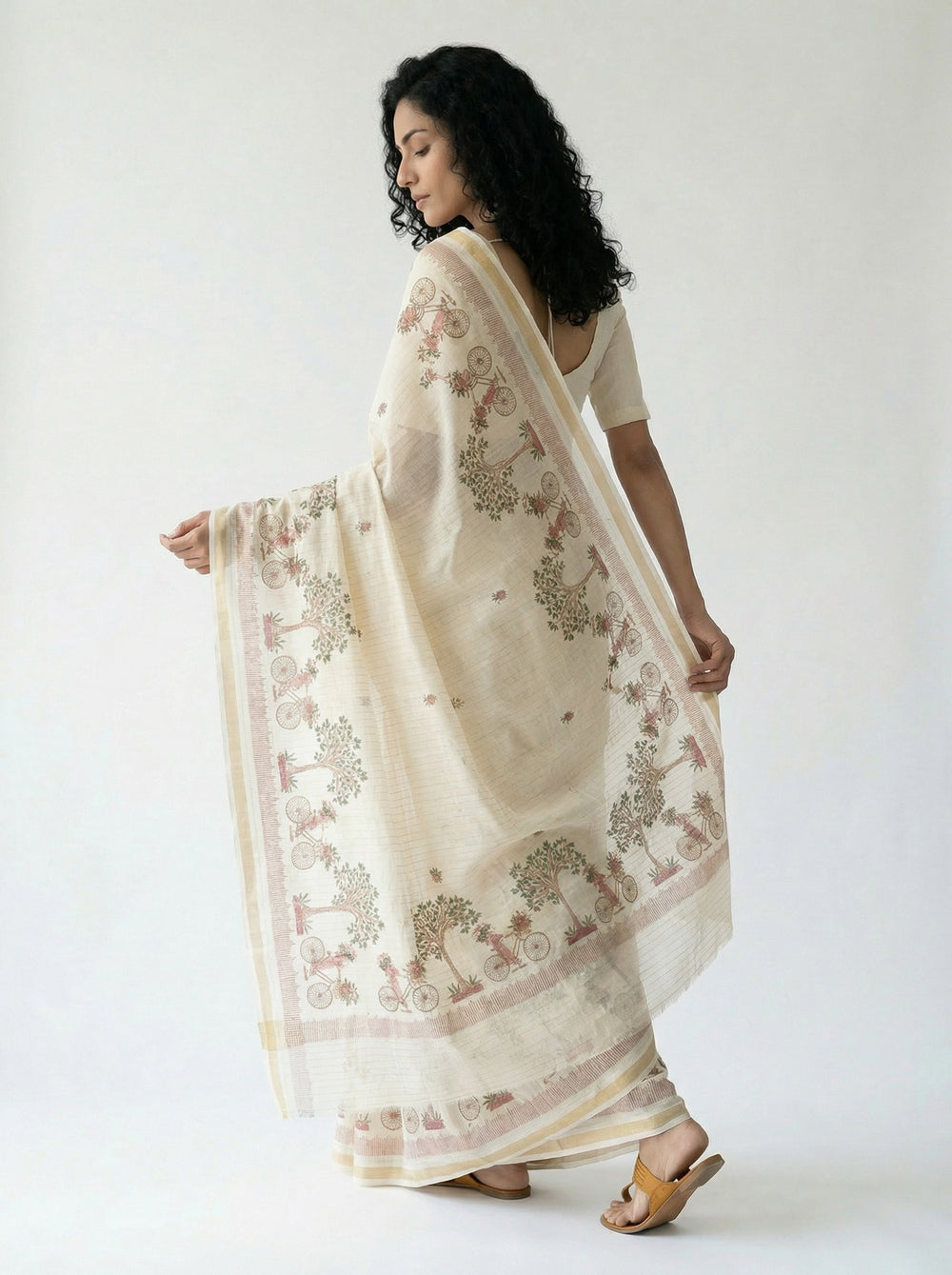 Woman in a traditional saree standing in a room with wooden furniture and decor.