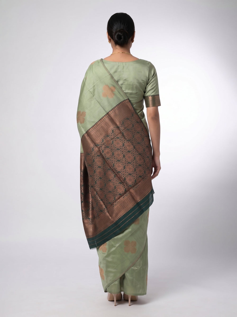 Woman in a green saree standing in a well-furnished room with books and decor.