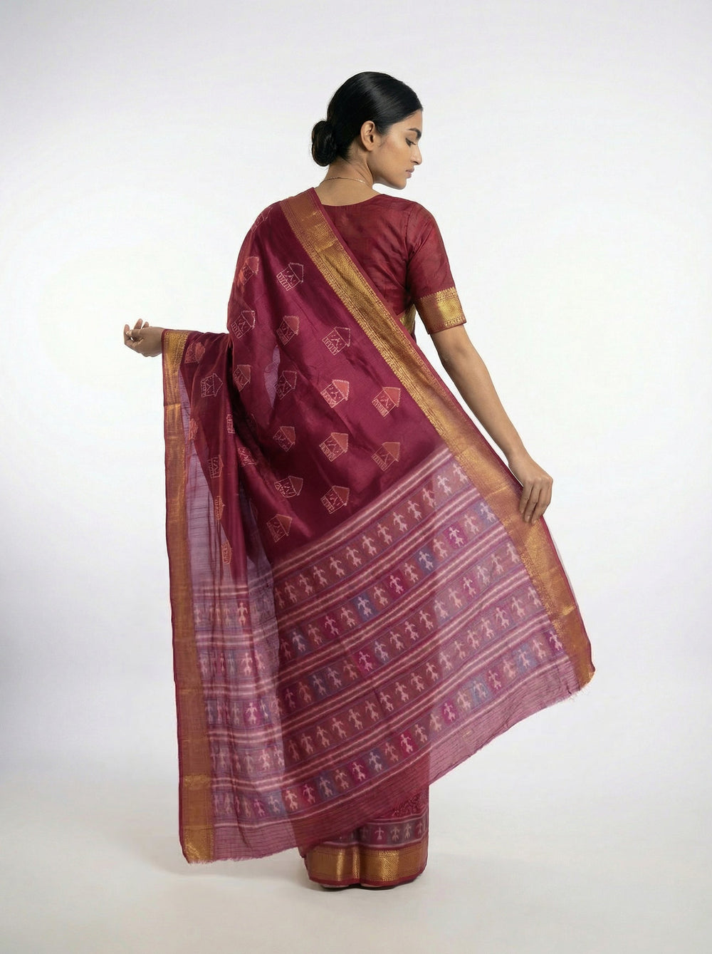 Woman in a traditional maroon saree standing on a balcony with plants and a wooden railing.