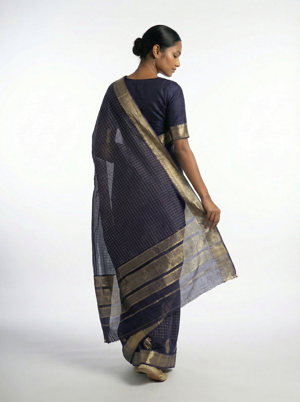 Woman in a traditional blue saree with gold accents standing in a sunlit room with arches.