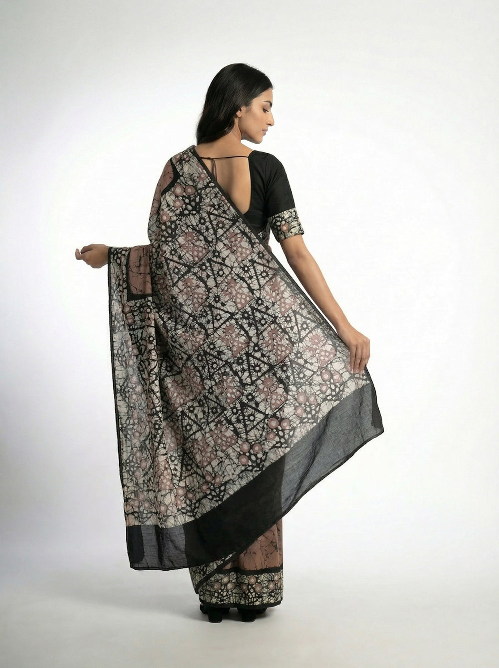Woman in a brown saree with black and white patterns standing on a stone path.
