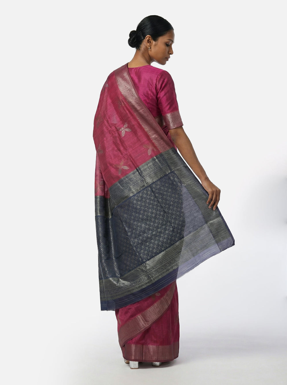 Woman wearing a pink saree with a patterned border against a pink background