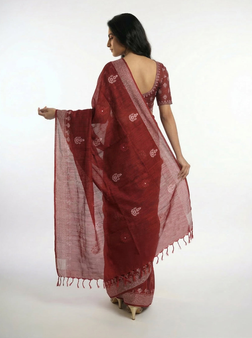 Woman in a red saree standing in a room with a window and table.